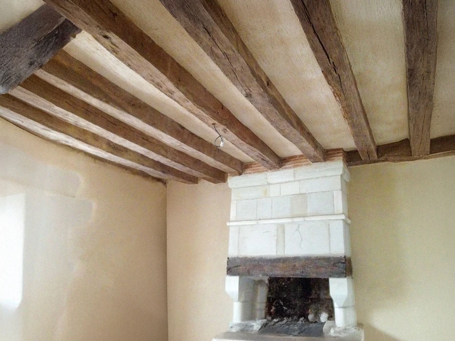 Intérieur rénové avec cheminée en pierre blanche et poutre de manteau en bois brut