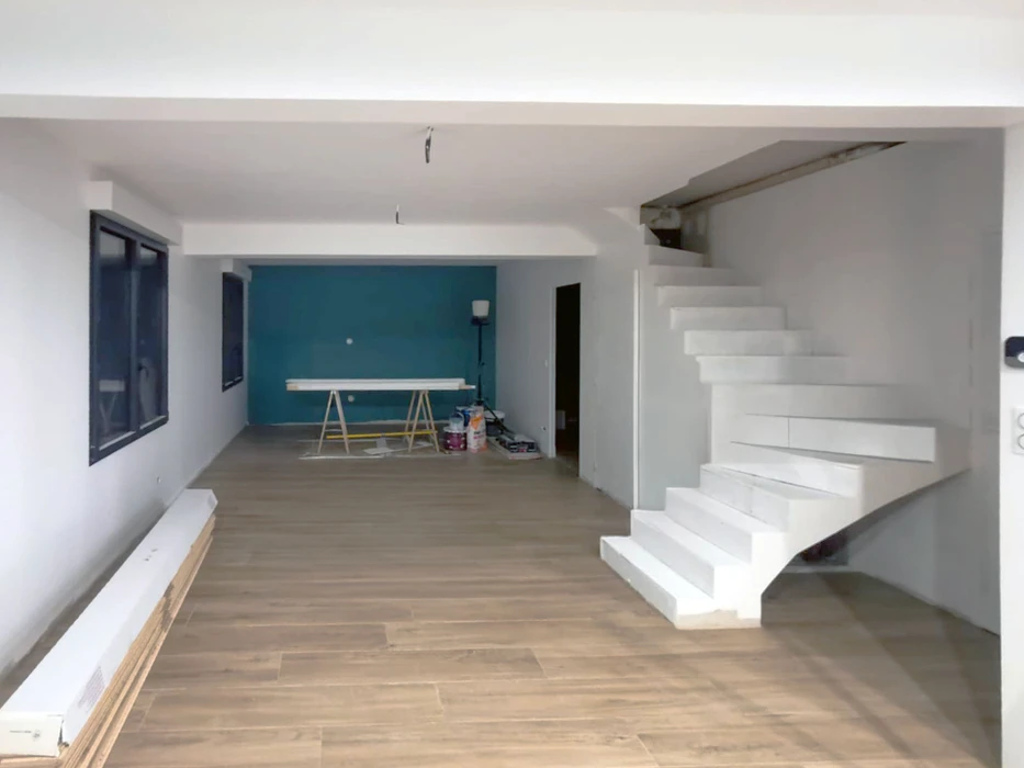 Intérieur moderne en cours de finition avec escalier suspendu blanc, mur d'accent bleu-vert, sol stratifié bois clair