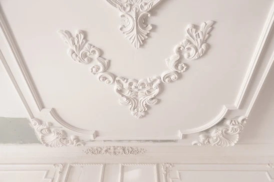 Plafond intérieur avec moulures décoratives en plâtre blanc ornées de motifs floraux et volutes baroques